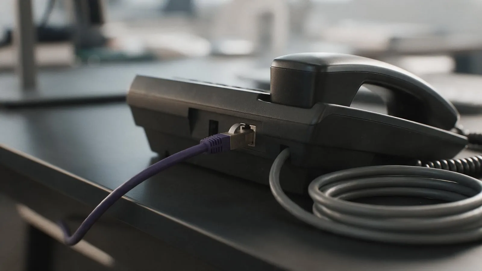 Macro of a network cable plugged into the back of a desk phone